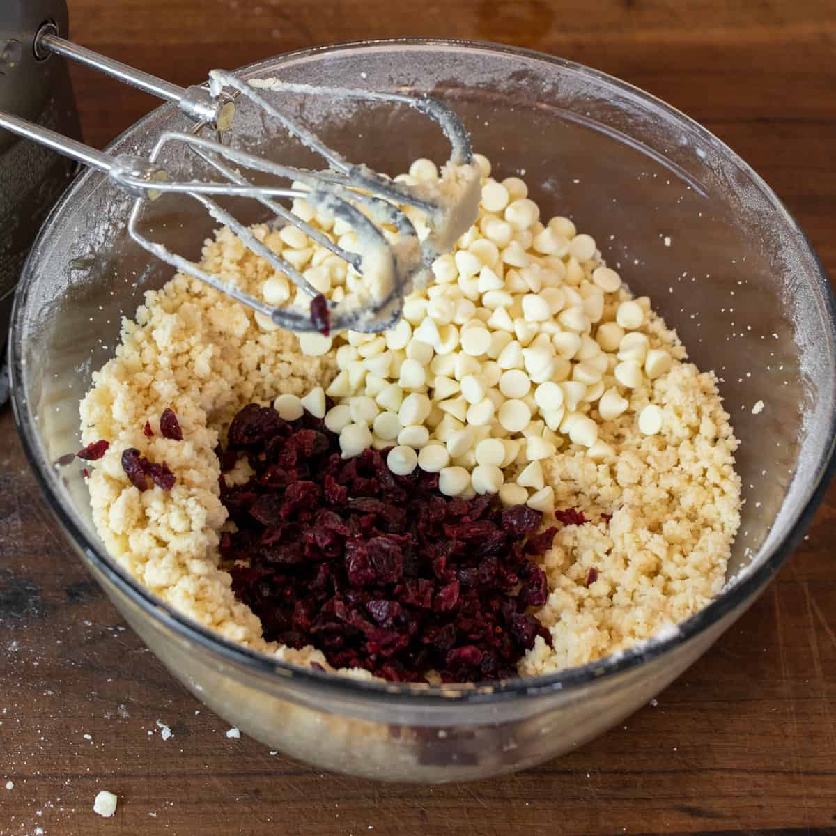 Dried cranberries and white chocolate chips added to a mixing bowl with cookie dough.