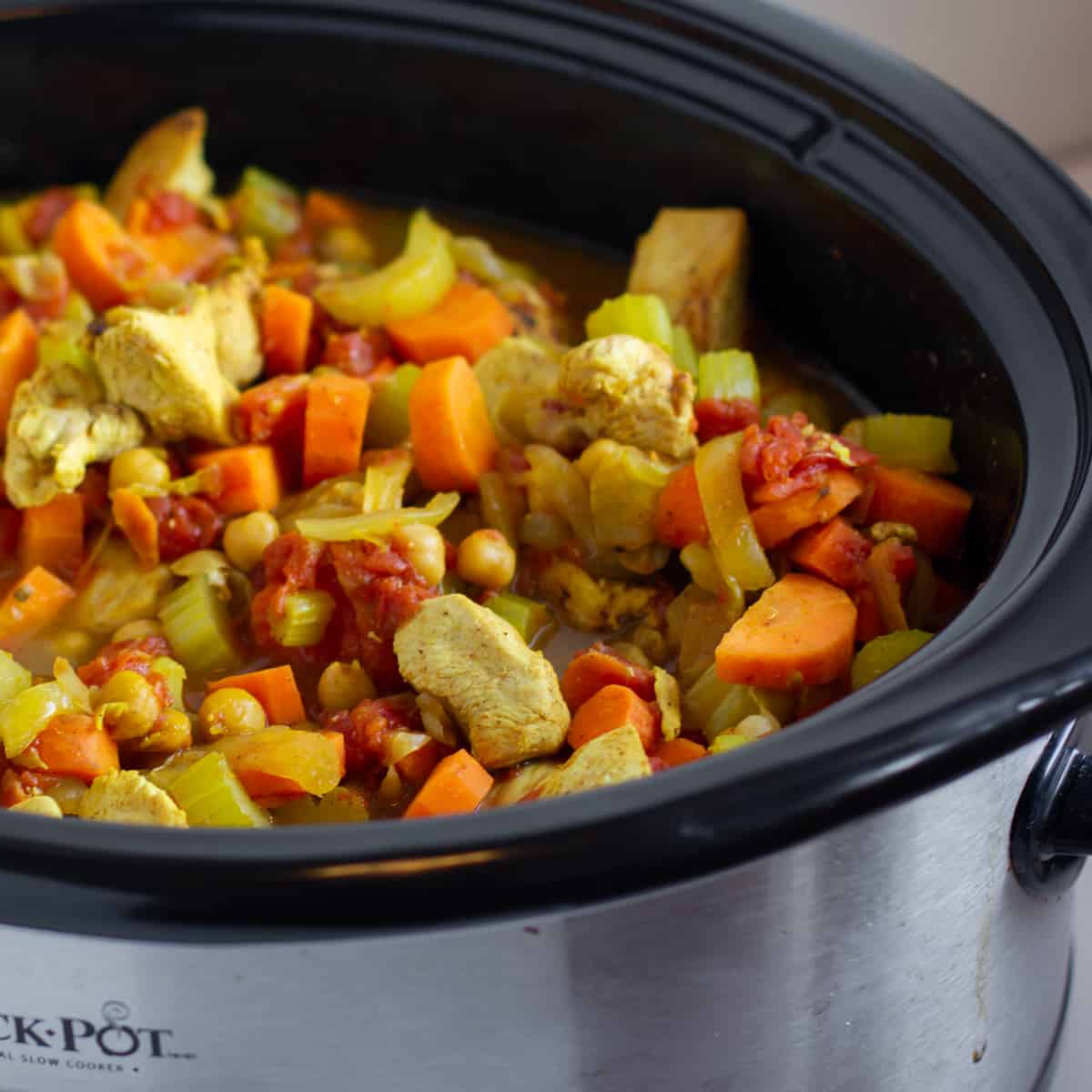 A slow cooker with chicken and raw vegetables.