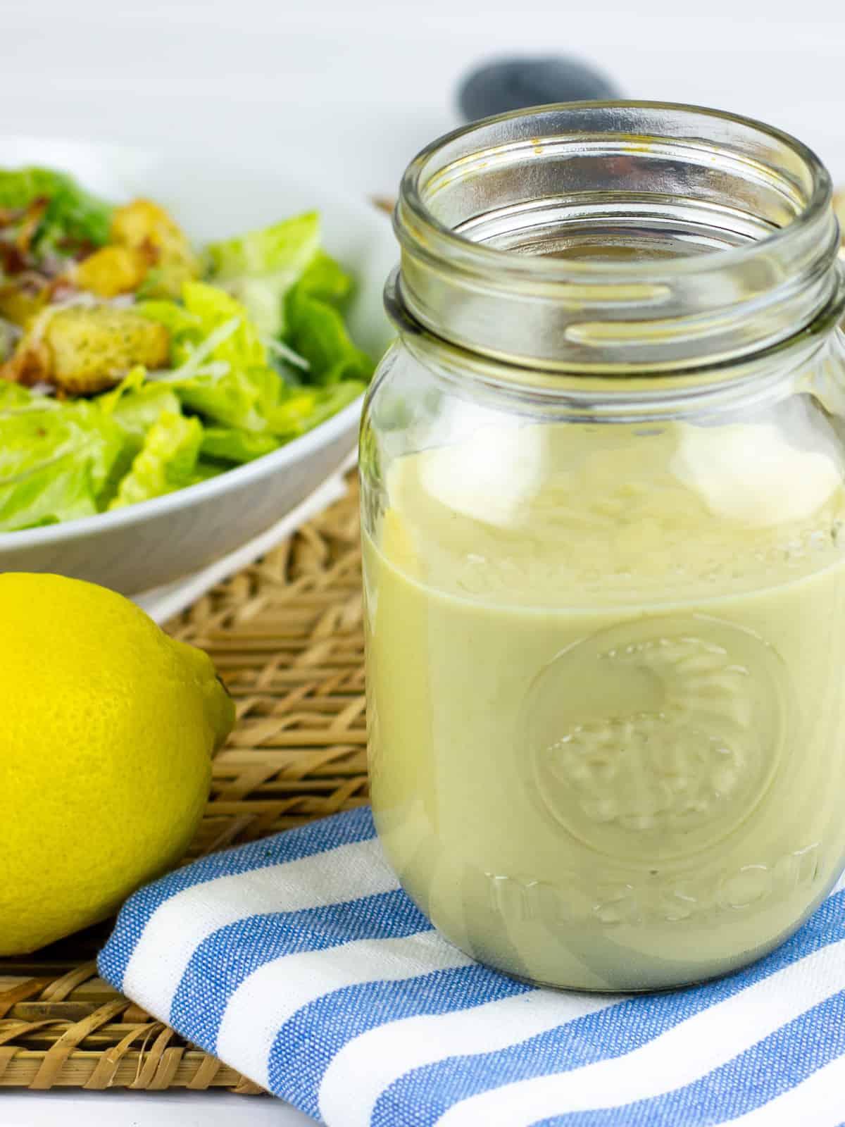 A jar of dressing in front of a bowl full of salad.