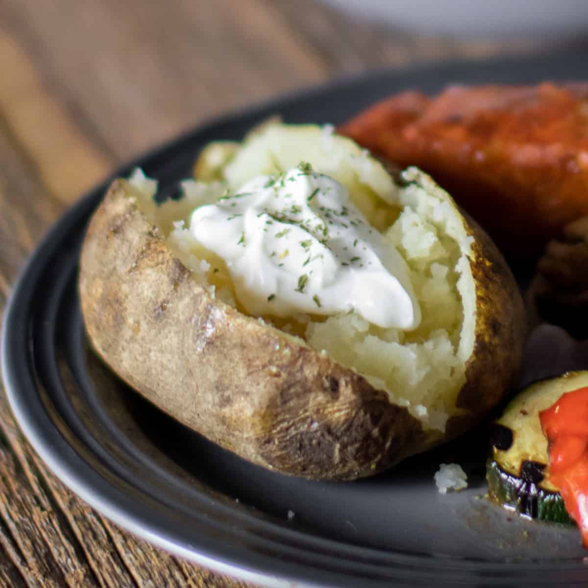 A baked potato on a plate split open with a dollop of sour cream.