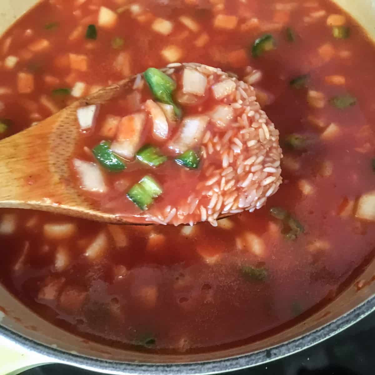 A wooden spoon lifting up rice, peppers and onion out of a pot.