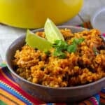 A bowl of mexican rice with a couple lime wedges.