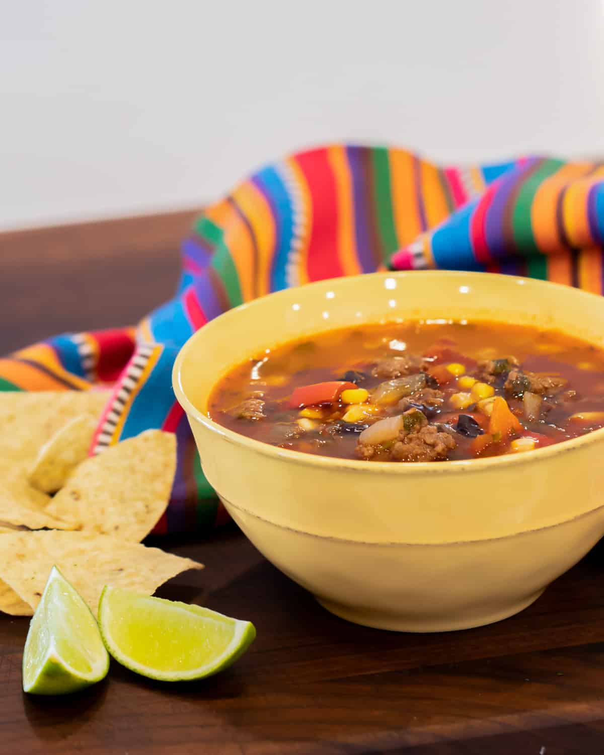 A yellow bowl with soup with lime wedges  and a colourful napkin.