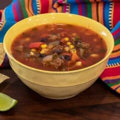 A bowl of soup next to lime wedges and tortilla chips.