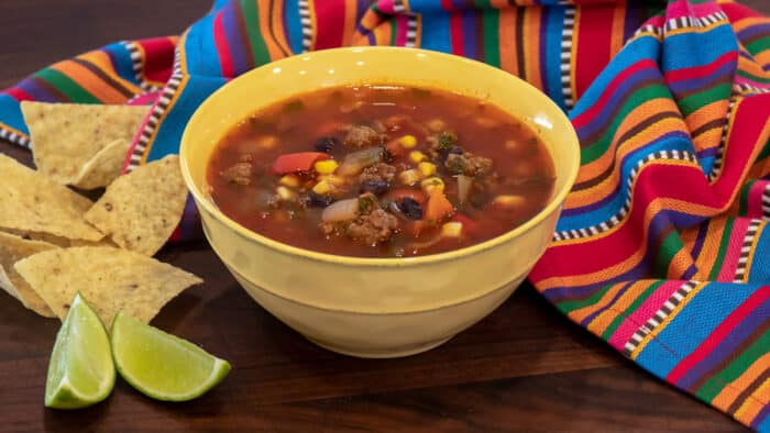 A bowl of soup next to lime wedges and tortilla chips.