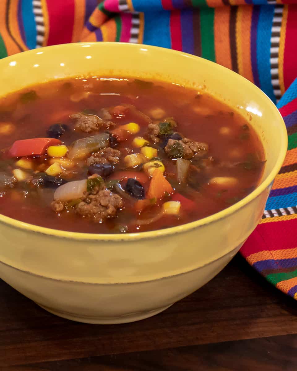 A bowl of soup with ground beef, corn and black beans.