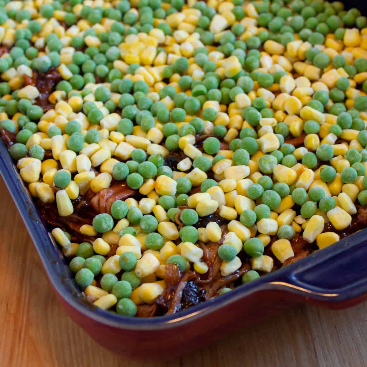 Frozen peas and corn spread over cooked meat.