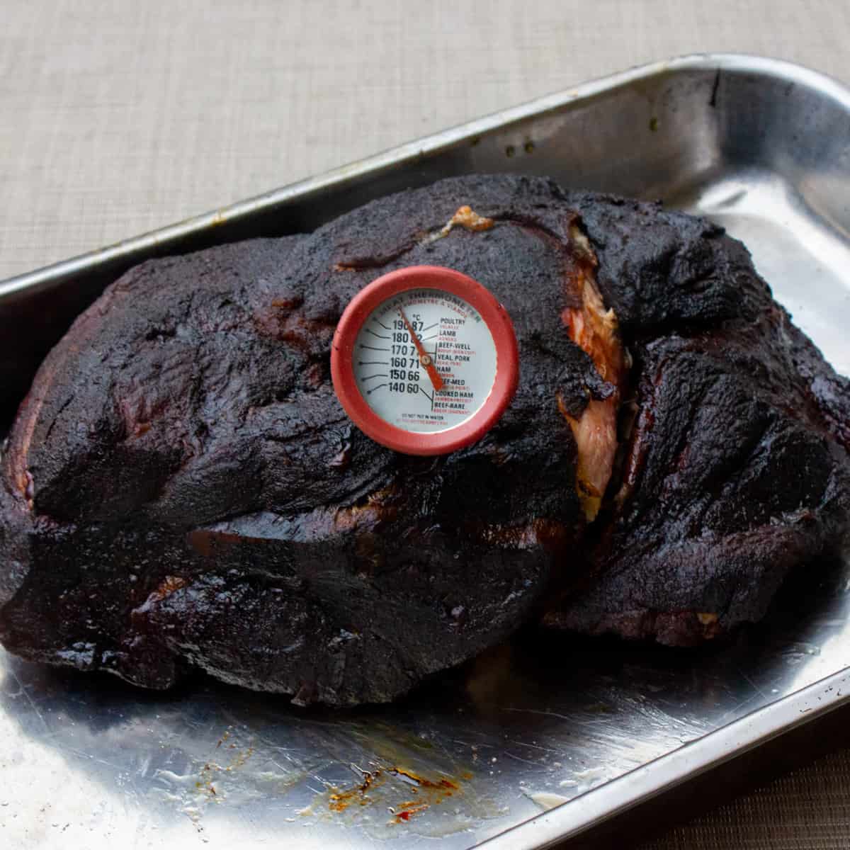 A cooked pork butt with a thermometer inserted into the meat.