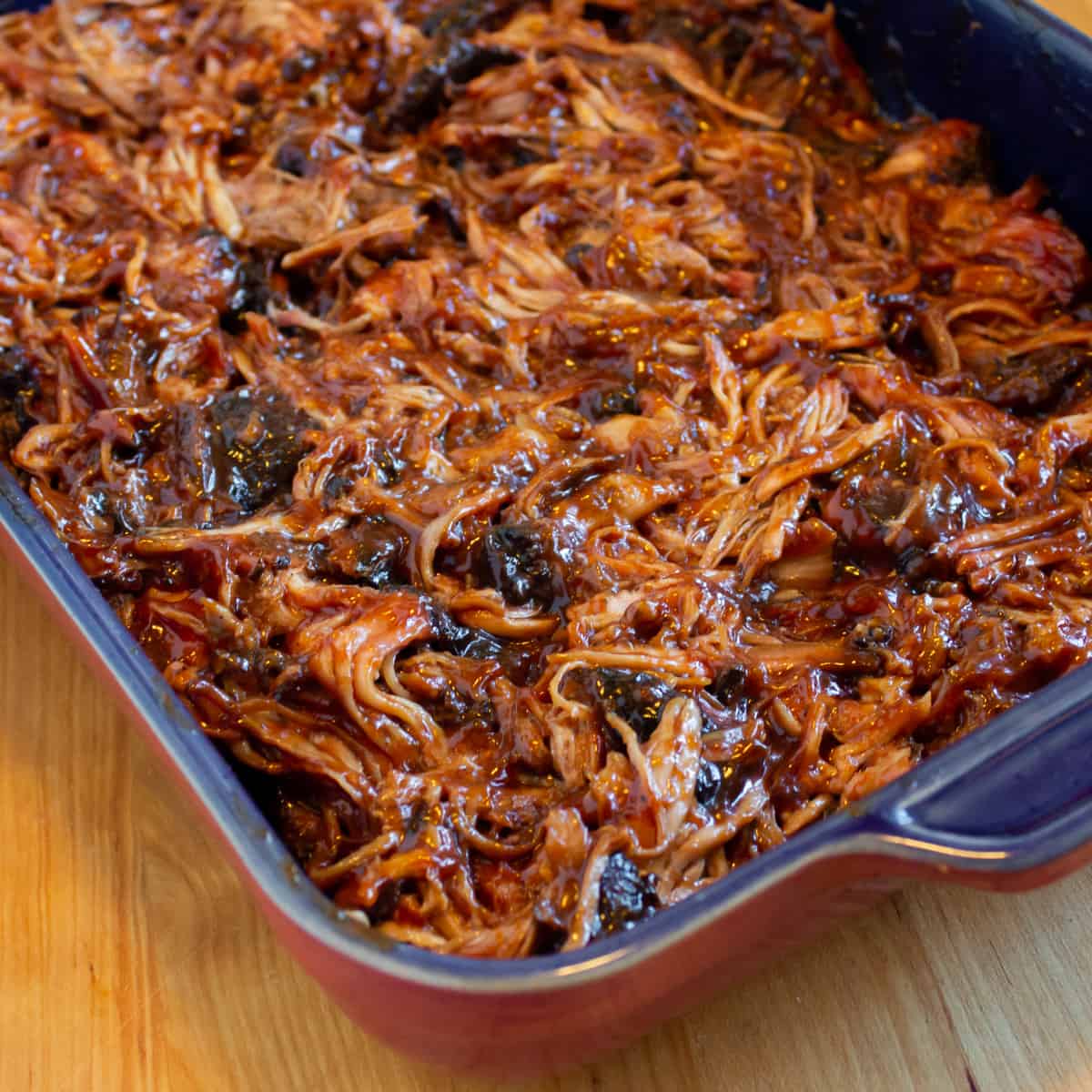 Shredded pork meat mixed with BBQ sauce and spread in a baking dish.