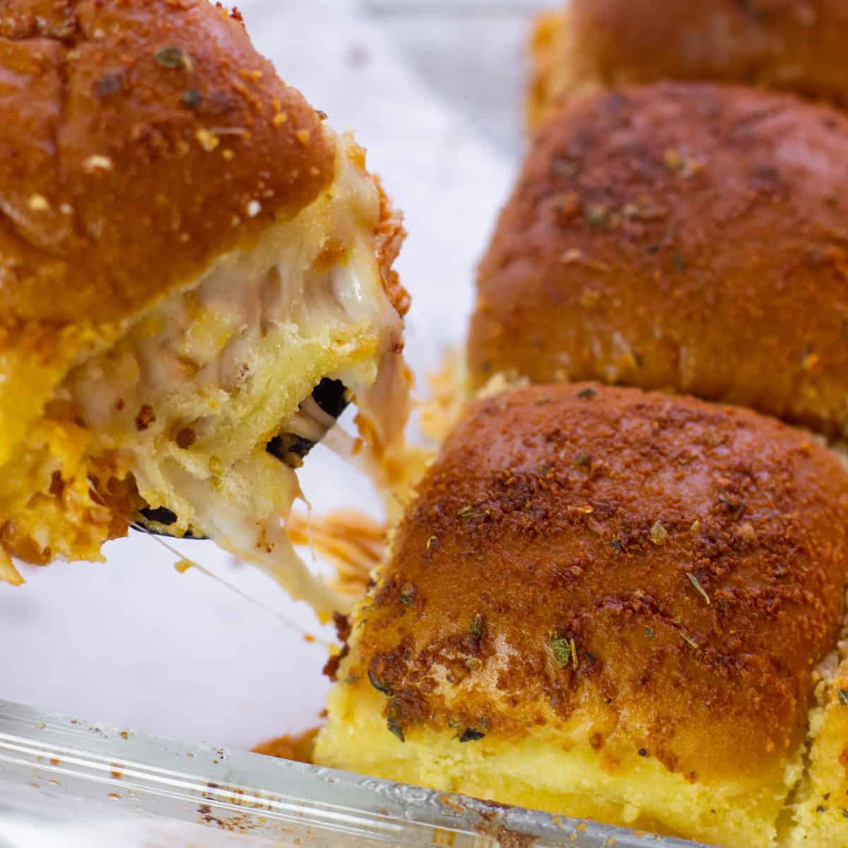 A hot slider being removed from a baking dish with the melted cheese stretching.