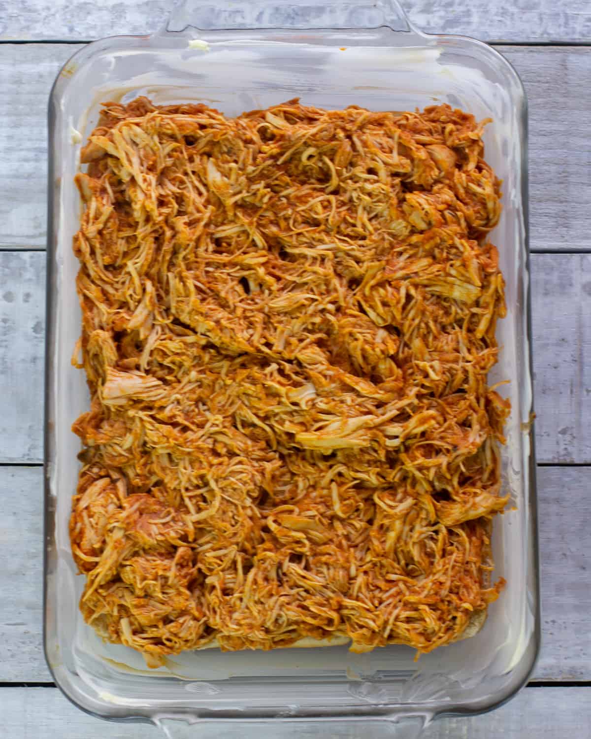 A baking dish with pulled chicken on dinner rolls.