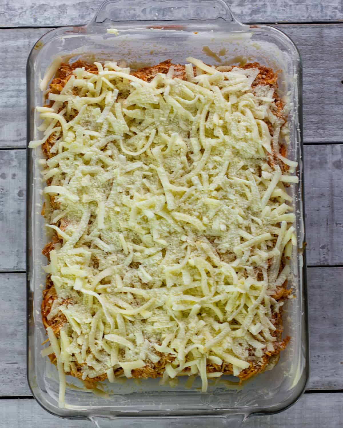 A baking dish with chicken and grated cheese.