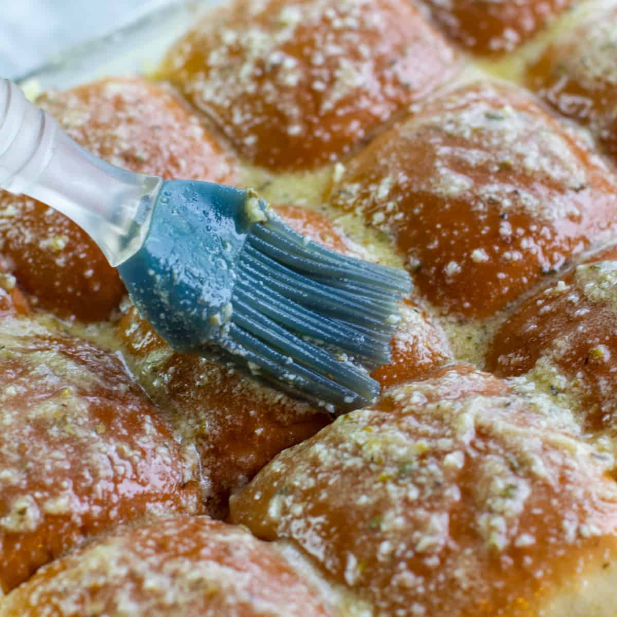 Melted butter and parmesan being brushed on dinner rolls.