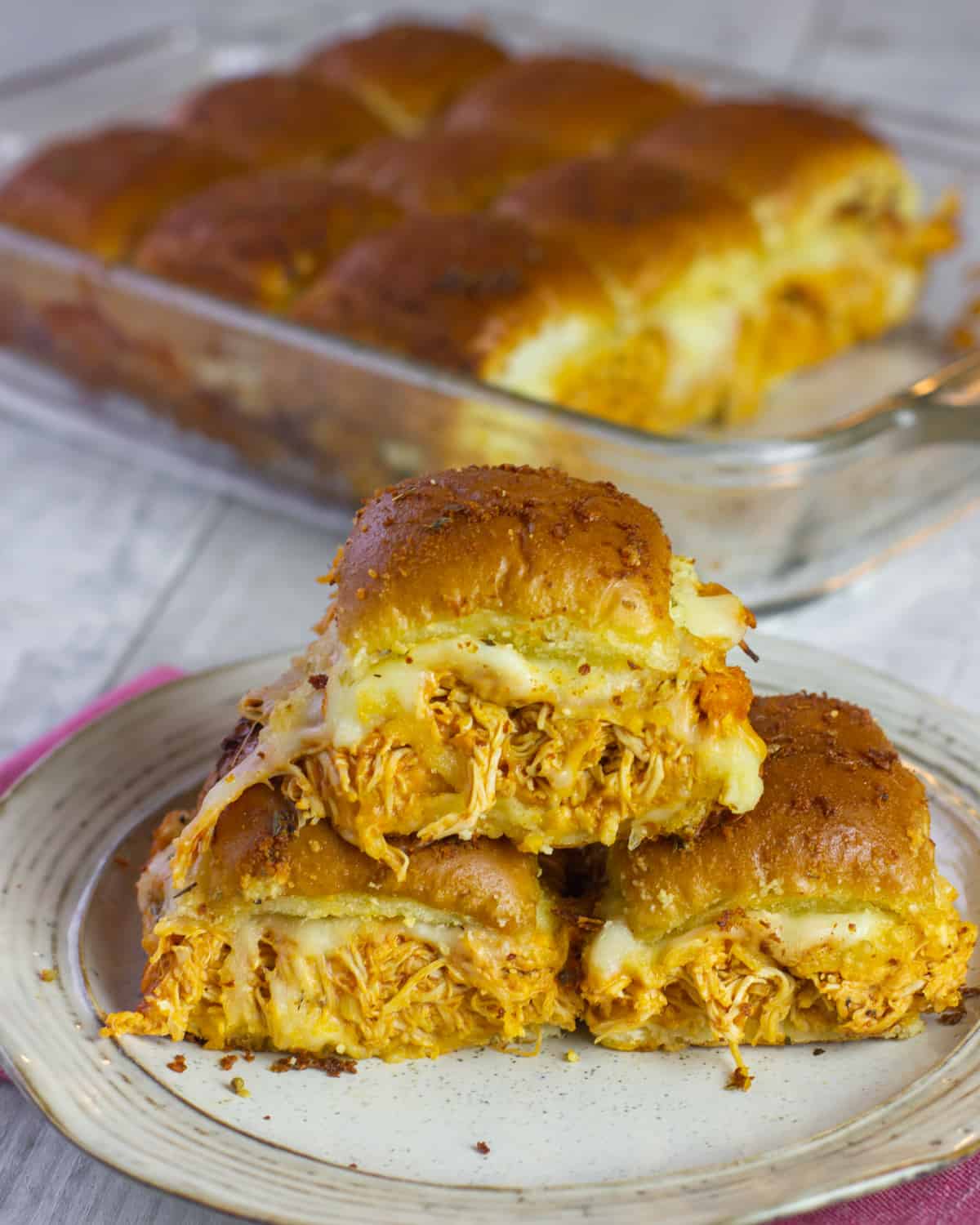 Chicken sliders on a plate with more in a dish behind.