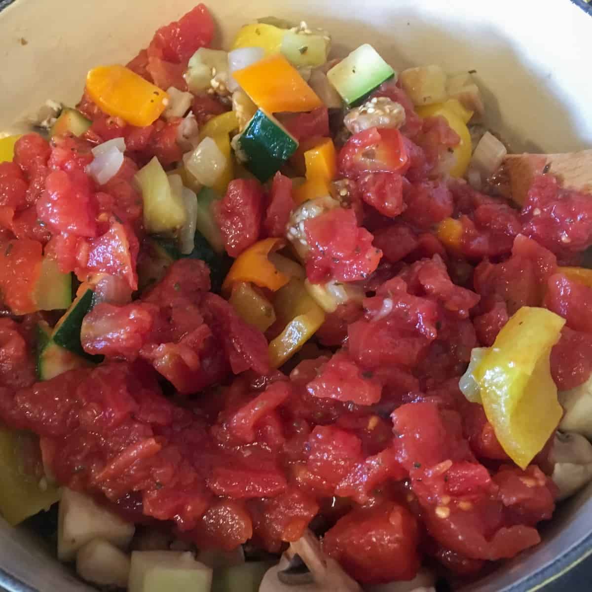 A can of diced tomatoes dumped into a pot with other vegetables.