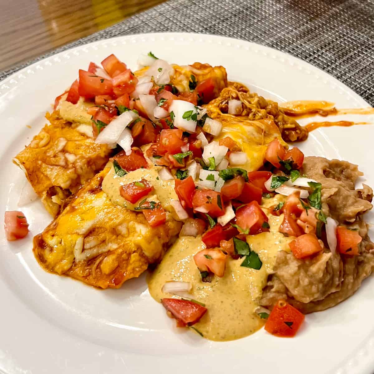 Baked enchiladas on a plate with pico de Gallo, refried beans and sauce.
