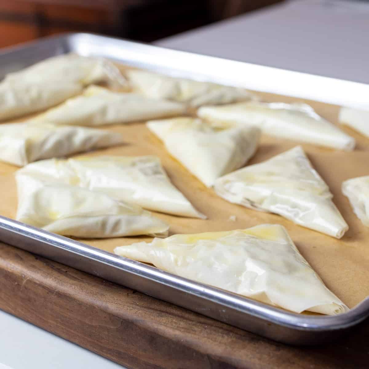 Phyllo triangles on a baking sheet ready to go in the oven.