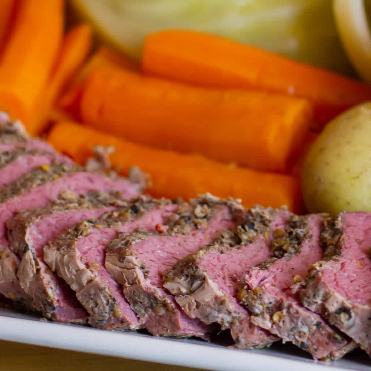 Sliced beef on a platter with carrots and potatoes behind.