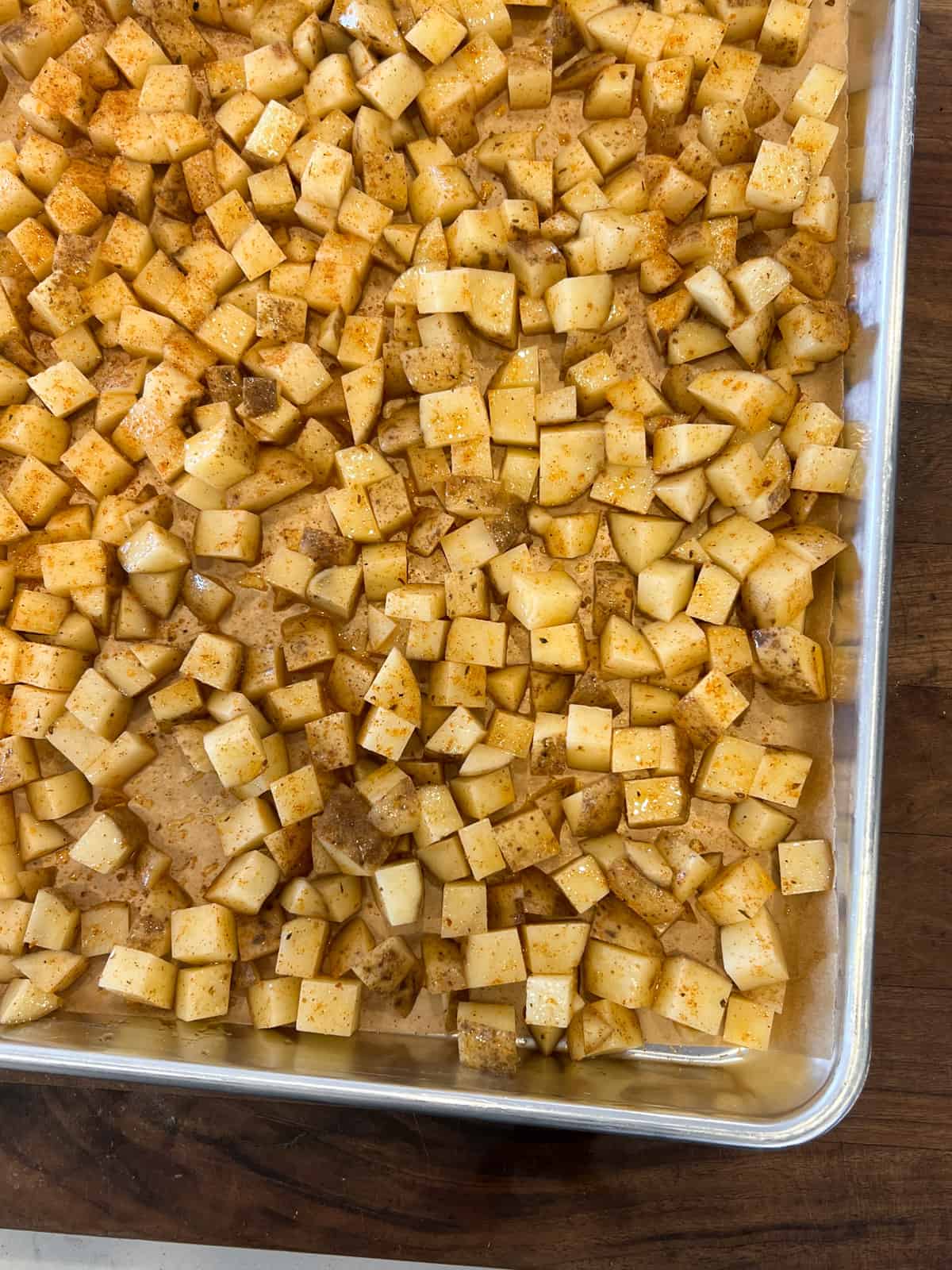 Diced raw potatoes seasoned and spread out on a baking sheet.