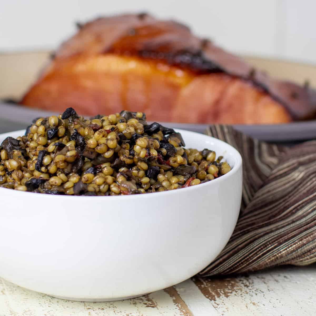 Wheat berries in a white bowl in front of baked ham.