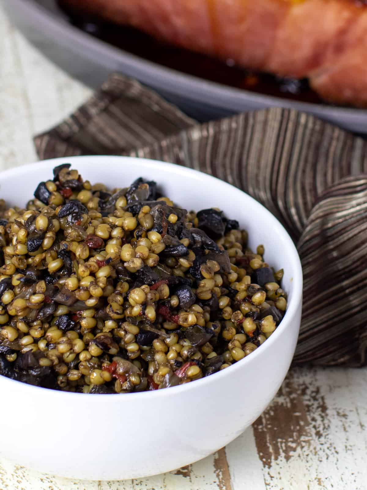 A bowl of a side dish in front of a baked ham.