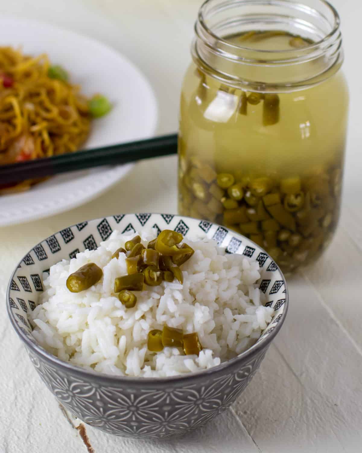 A small bowl of white rice with a few green chilli peppers on top.