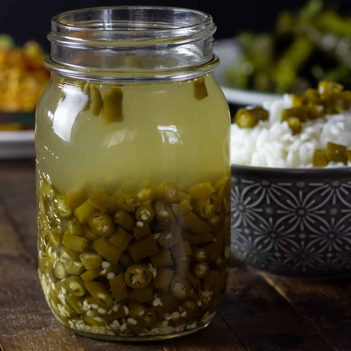 A jar of pickled green chillies in front of a bowl of rice.