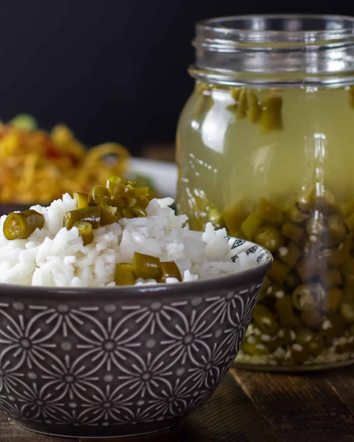 A close up picture of a bowl of rice with green chillies on top.