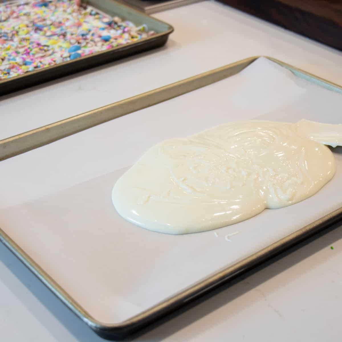 Melted white chocolate being poured on a baking sheet.