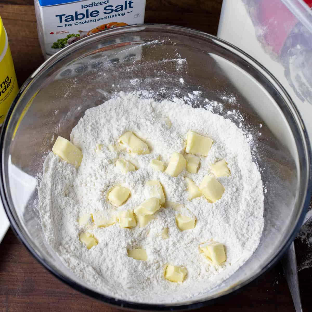 Butter cubes with flour in a large glass mixing bowl.