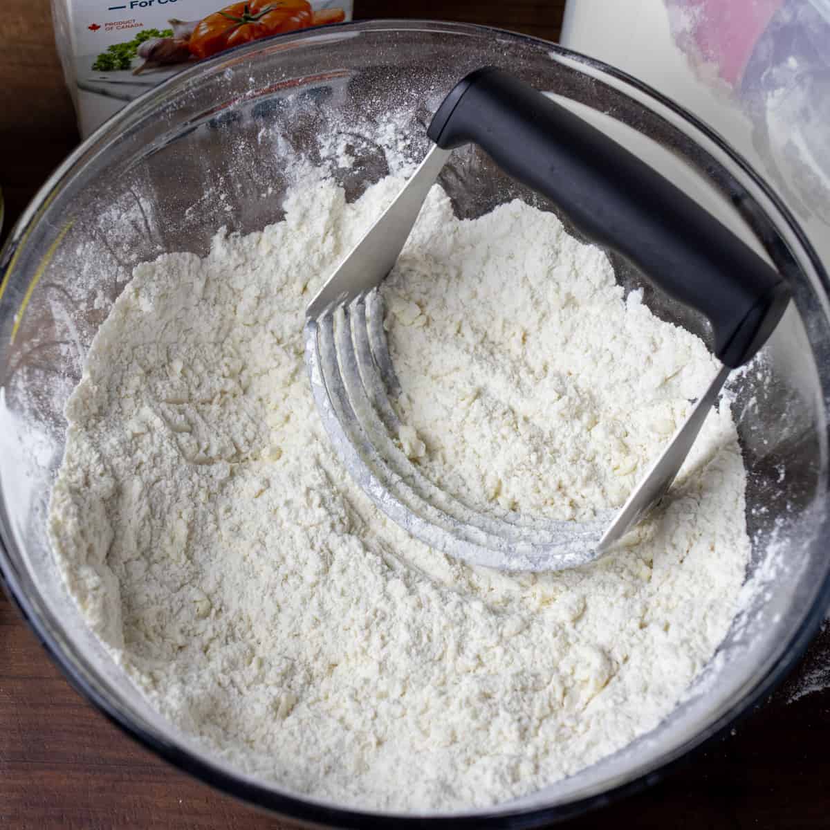 A pastry cutter in a glass mixing bowl after cutting butter into the flour.