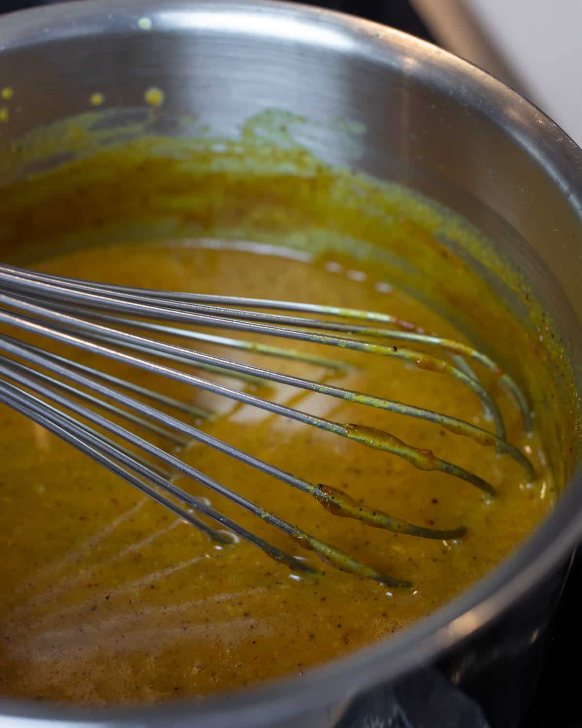 A whisk in a saucepan after mixing the sauce.