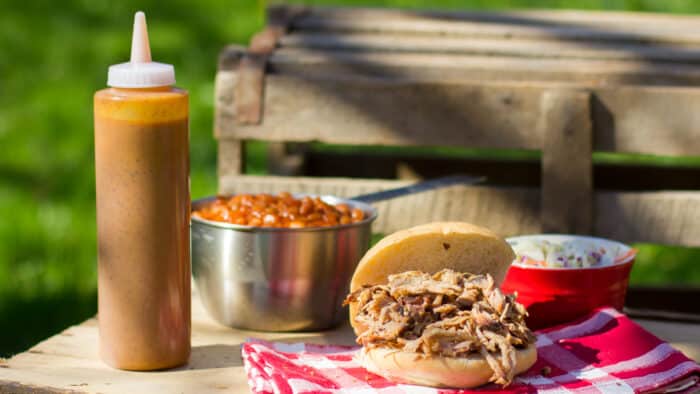 A bottle of mustard sauce next to pulled pork on a bun.