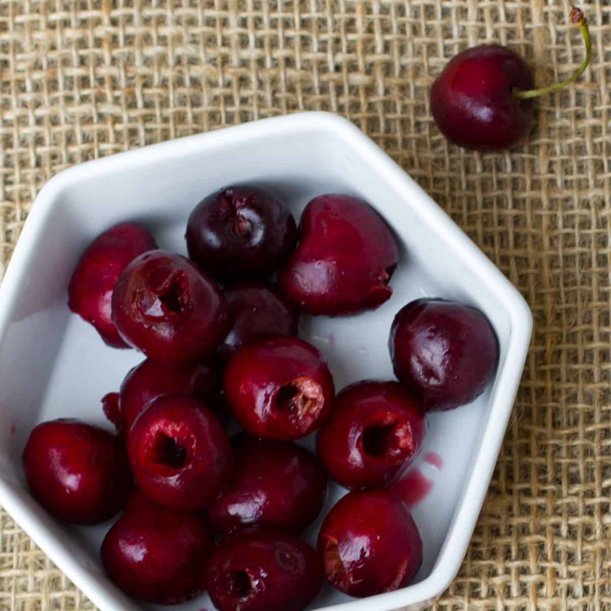 Pitted cherries in a white hexagon shaped bowl.
