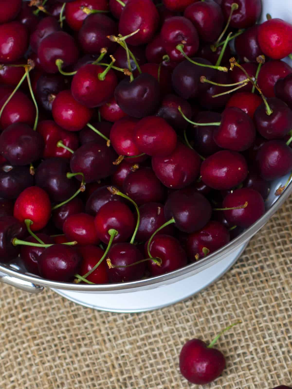 A white strainer filled with cherries.