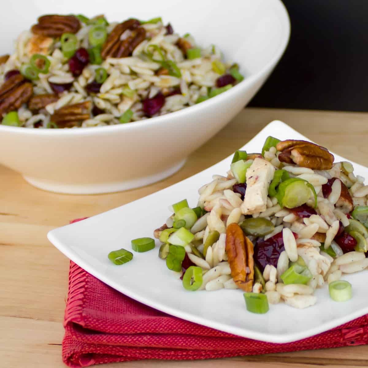 Pasta salad on a white plate in front of a full bowl of salad.