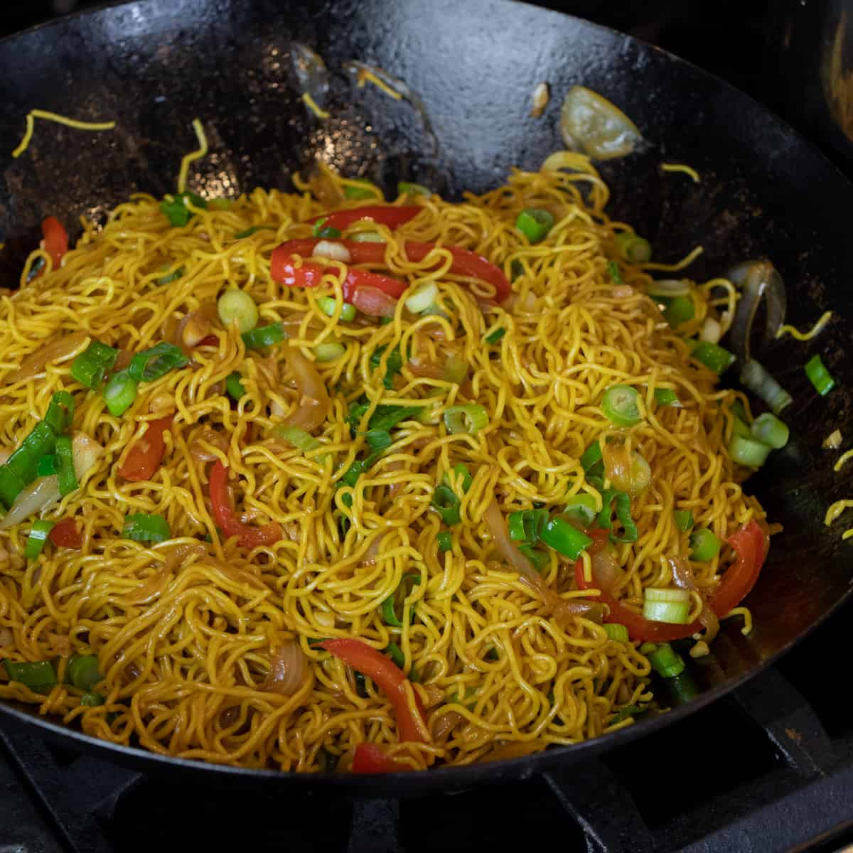 Noodles in a wok with peppers and green onions.