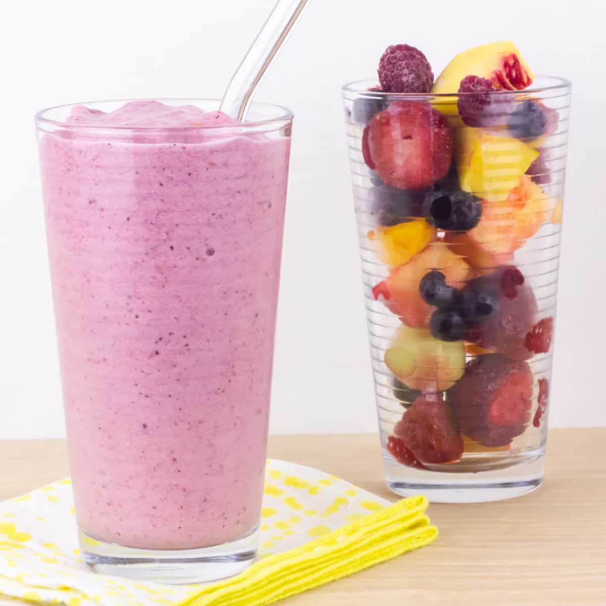 Two glasses next to each other. One with a smoothie and the other with frozen fruit.