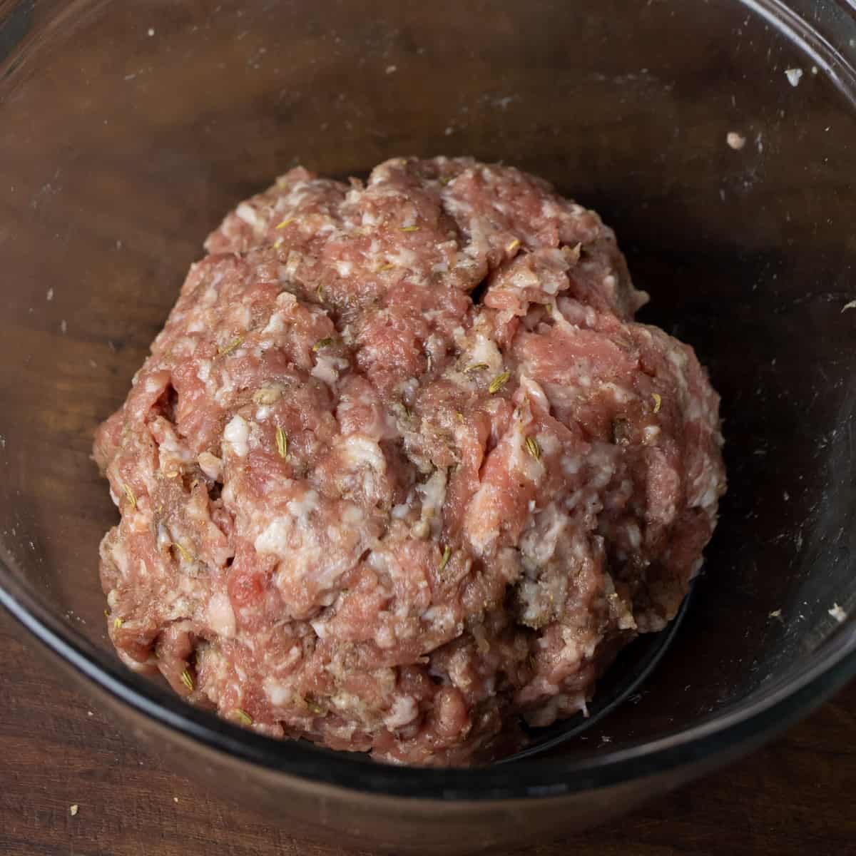 Raw sausage meat in a glass mixing bowl.