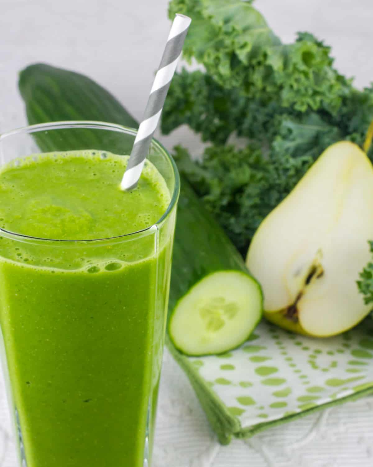 A glass full of smoothie next to fruits and vegetables.