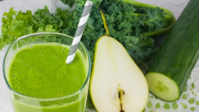 A close up picture of a smoothie in a glass and a sliced pear.