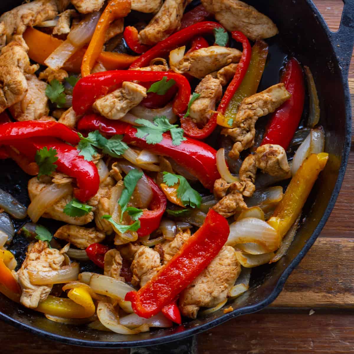 A cast iron skillet with sautéed chicken, onions and peppers.