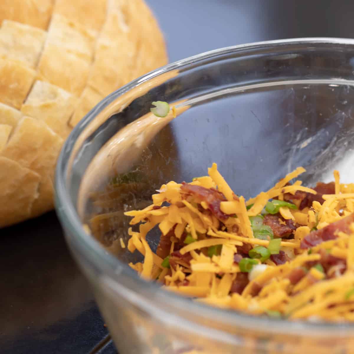 A glass mixing bowl with bacon, grated cheese and sliced green onions.