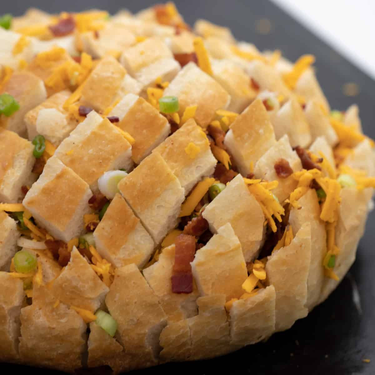 A round loaf of bread with cheese, bacon and onions stuffed through the slits all throughout the bread.