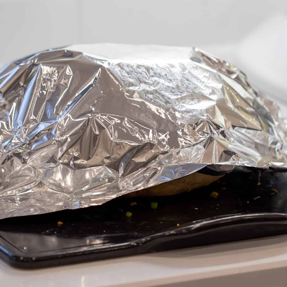 Aluminum foil covering a loaf of bread on a baking stone.