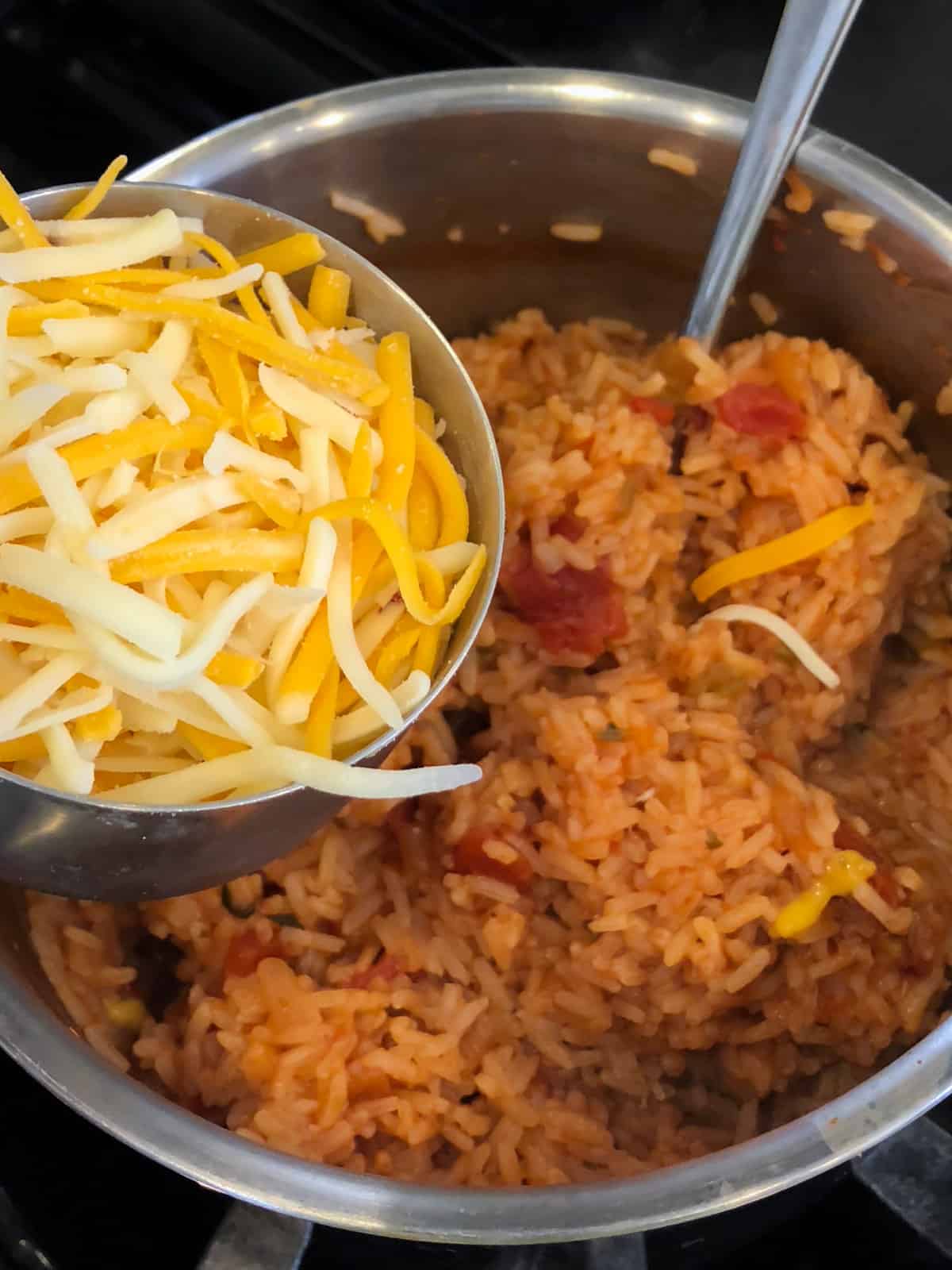 A measuring cup of grated cheese being dumped into a pot of cooked rice.