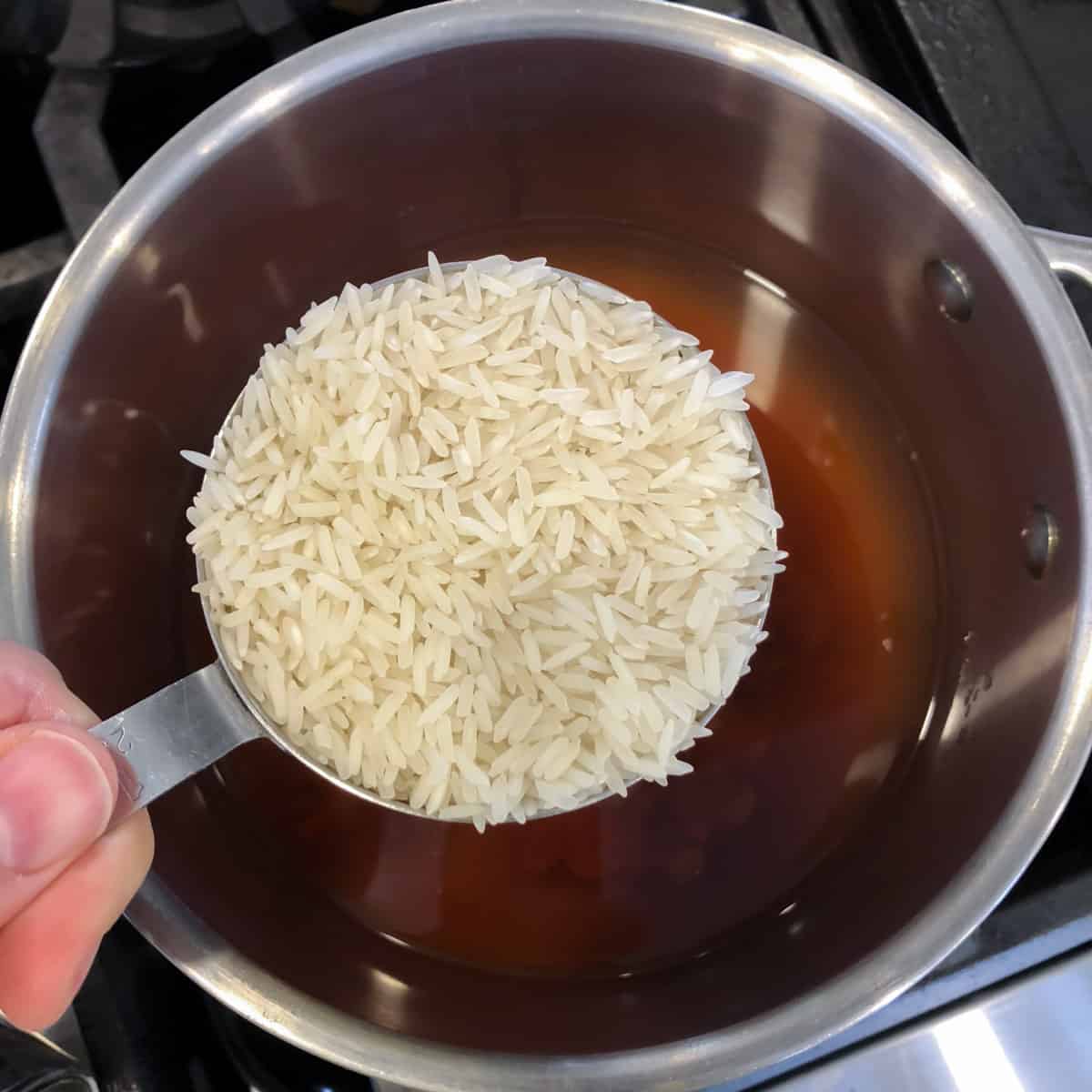 A measuring cup with uncooked rice over a pot.