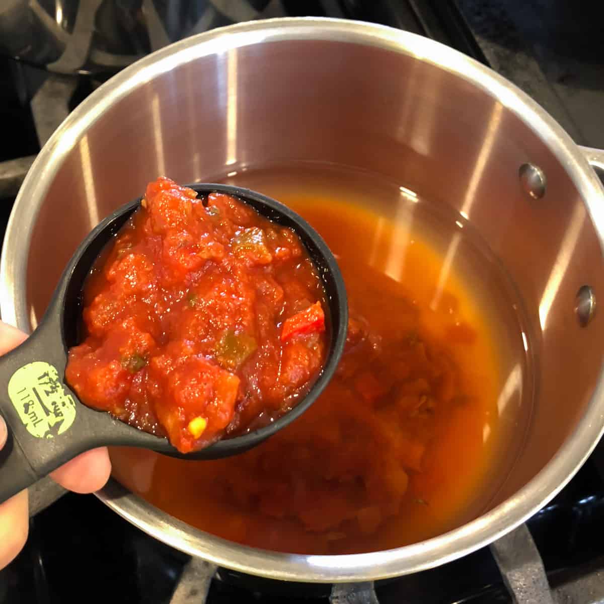 A measuring cup with salsa over a pot.