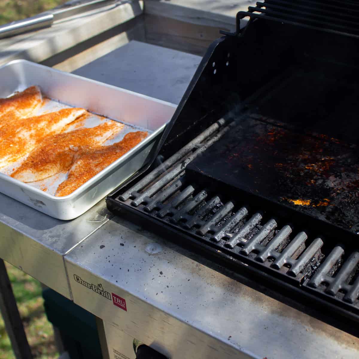 Grill with cooking stones on the grate and a tray of raw fish on the shelf.