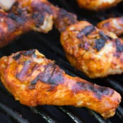 Chicken drumsticks cooking on a grill.